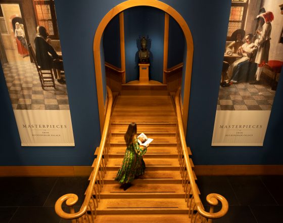 A member of Royal Collection Trust staff undertakes final checks on exhibition, standing on staircase inside Queen's Gallery.