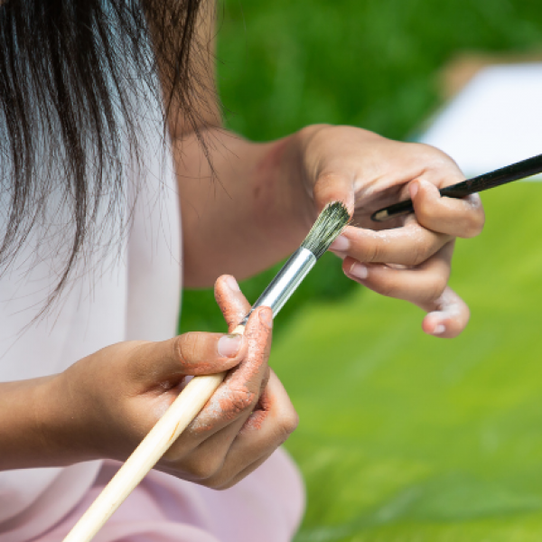 Young artist holds paintbrushes.