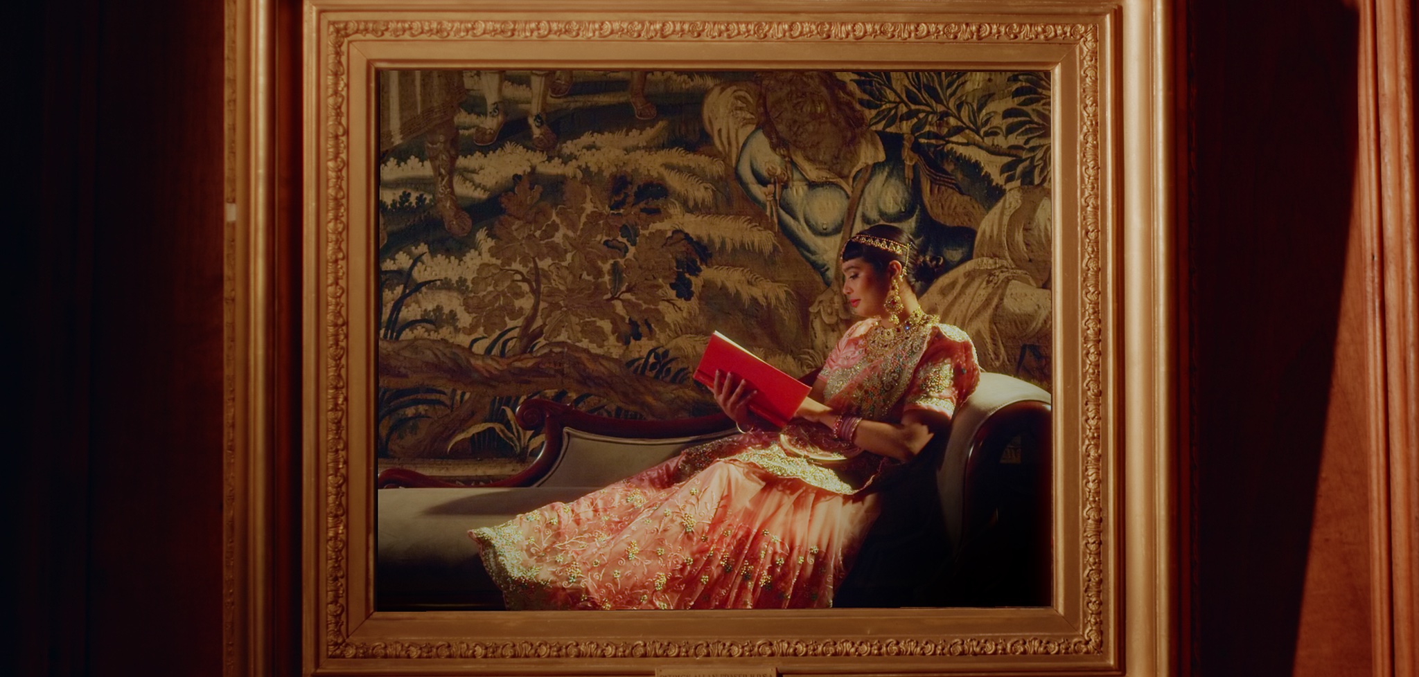 Picture frame showing person relaxing with book, set against richly decorated tapestry.