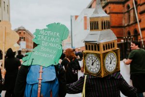 Scene of a demonstration with people holding cardboard cut-outs of Ireland and Big Ben.